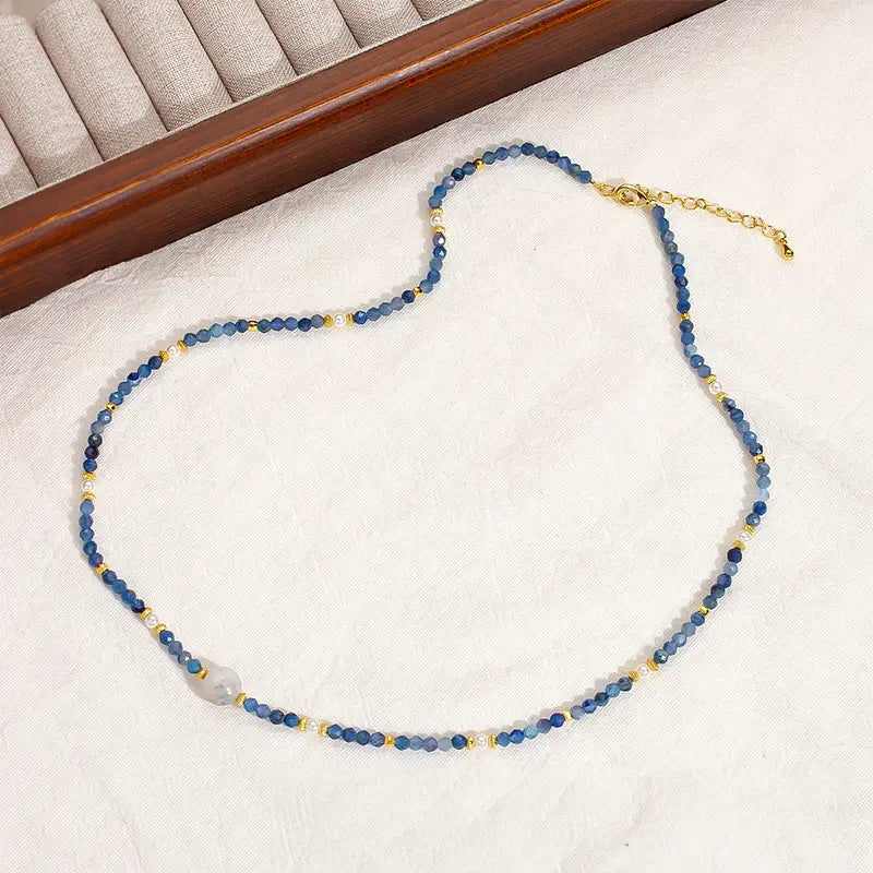Camile Turquoise Lapis Lazuli Pendant Necklace with blue beads and gold accents on beige.