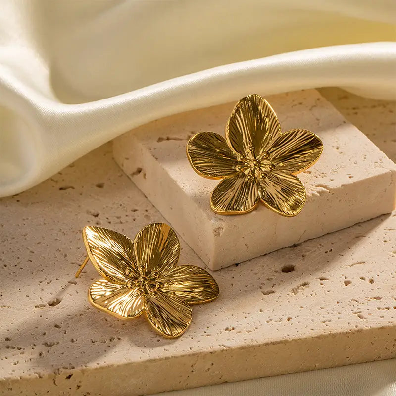 Gold Fleur de Lune Plumeria Earrings with detailed petals on stone and ivory fabric