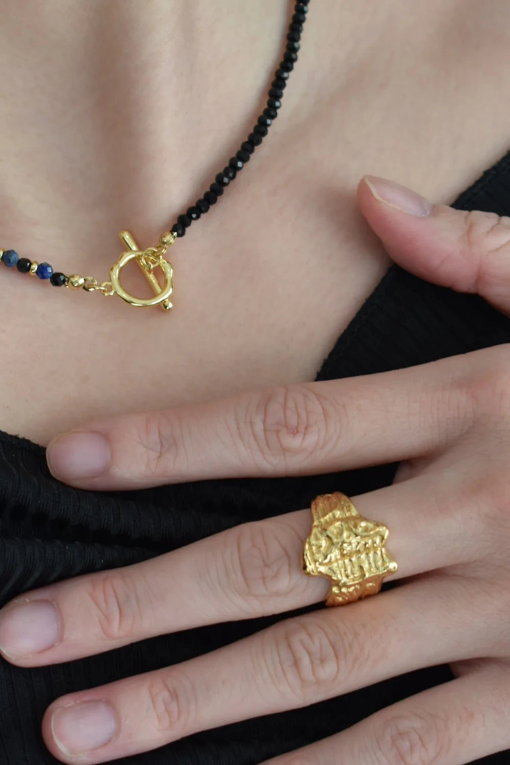 Model wearing Erosia gold ring and black bead necklace with textured finish