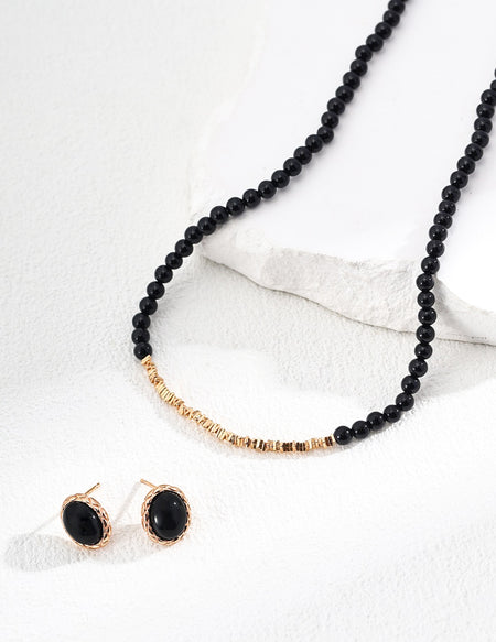 Matching black agate earrings and necklace set with gold accents, elegantly displayed on a textured white surface.