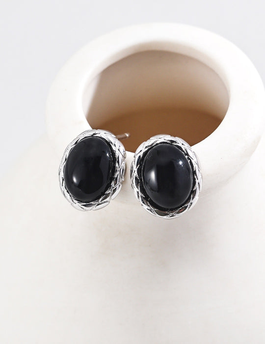 Sophisticated black agate earrings set in silver with a woven border, showcased on a white vase.