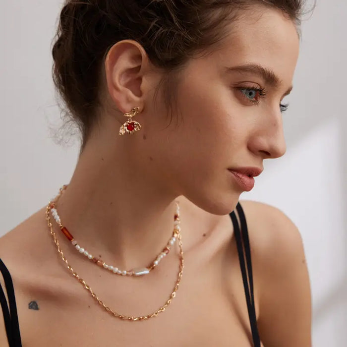 Close-up view of the Aimee Gold Agate Drop Earrings, highlighting the unique sculpted gold design and deep red agate stones, worn by a model.