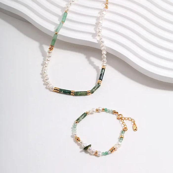 The primary necklace features a half-and-half design with one segment made of smooth, spherical white pearls and another of green crystal beads, segmented by gold-plated details. The complementary bracelet mirrors this design, showcasing a delicate interplay of pearls and green crystals with gold accents, creating a fresh, elegant look. 