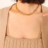 Close-up of a woman wearing a stylish gold link necklace. The necklace rests elegantly on her collarbone, complementing her beige ribbed sweater. The image highlights the smooth, reflective finish and intricate ball detailing of the links, emphasizing its chic and modern design.