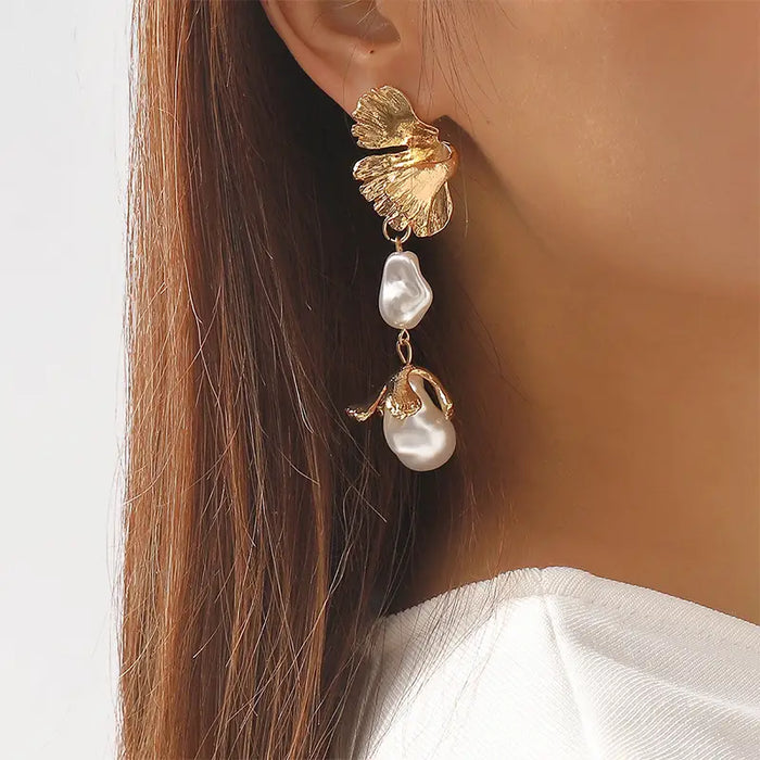 The earring features a golden leaf at the top, meticulously detailed to mimic the texture and veins of a natural leaf. Below the leaf, two baroque pearls are linked, each with an irregular but lustrous surface, adding an organic and elegant touch. The final element is a small, gold teardrop pendant, enhancing the earring's luxurious appearance. 