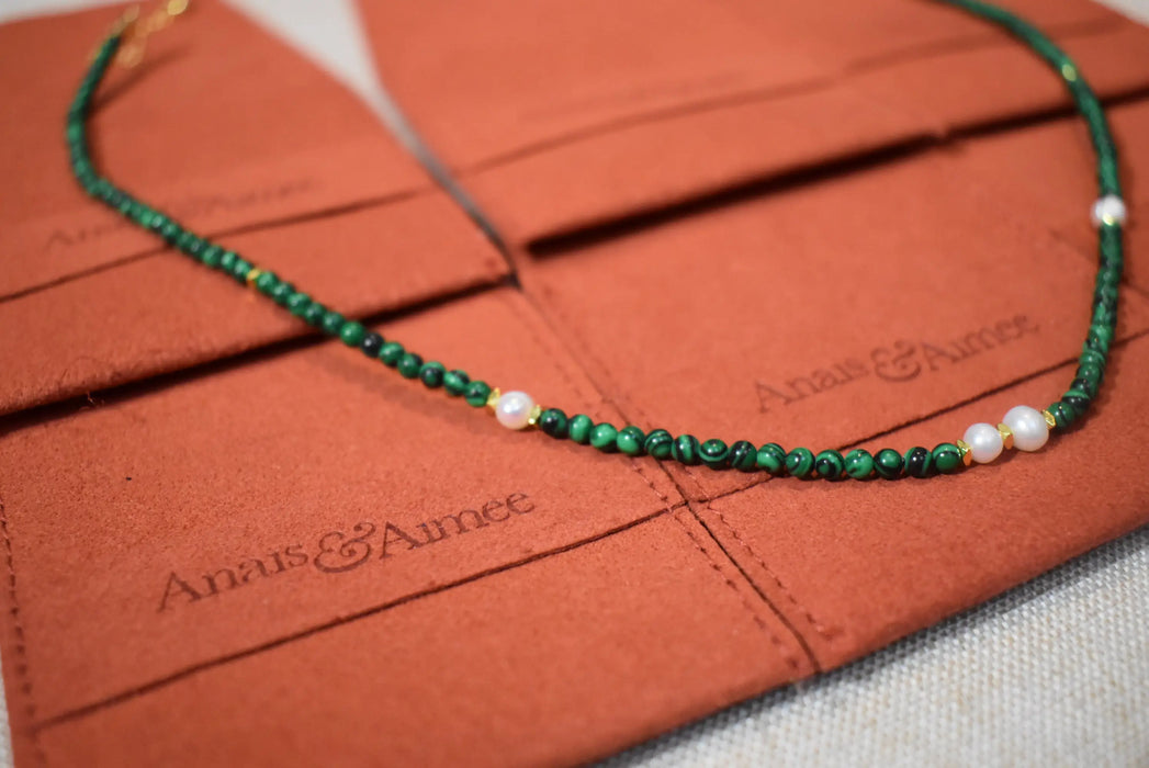 Close-up view of a malachite and freshwater pearl necklace placed on Anais & Aimee branded pouches, highlighting the intricate beads and luxurious finish.