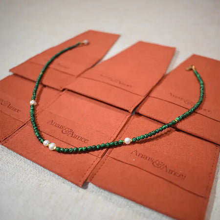 A malachite and freshwater pearl necklace arranged on brown jewelry pouches with gold-plated details.