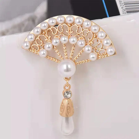 The design features an ornate, fan-shaped top embellished with multiple small pearls set in a golden frame, creating an intricate pattern. From the fan descends a larger pearl, followed by a decorative golden cap, and below it hangs a clear, elongated droplet. Just above the droplet, a small, round crystal adds a sparkling touch. The combination of pearls, gold, and crystal elements provides a rich, elegant look, suitable for formal occasions and sophisticated ensembles.