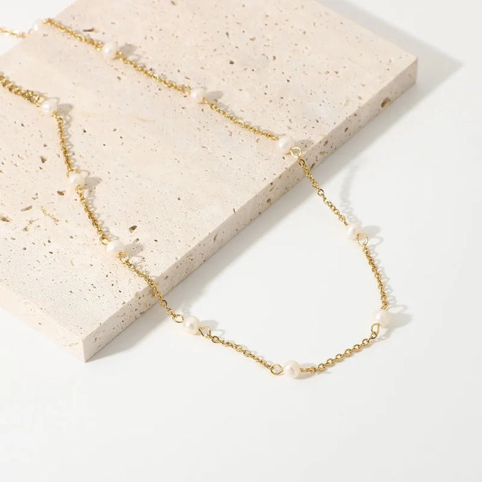 Aimee Gold Freshwater Pearl Chain Necklace delicately draped along a woman's neckline, featuring small, lustrous freshwater pearls evenly spaced on a fine gold chain, adding a touch of elegance to her look.