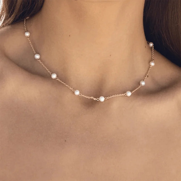 Aimee Gold Freshwater Pearl Chain Necklace delicately draped along a woman's neckline, featuring small, lustrous freshwater pearls evenly spaced on a fine gold chain, adding a touch of elegance to her look.