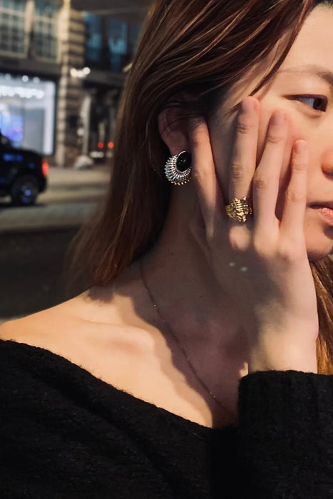 Model wearing Anaïs & Aimee black enamel statement earrings paired with the Erosia Organic Gold Statement Ring on a city street at night.