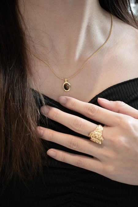 a model who are wearing a Anais & Aimee Tiger's Eye Pendant Necklace with a black outfit with wearing. a gold rings from anais & aimee 
