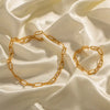 a gold paperclip chain bracelet and necklace gracefully placed on a smooth, lustrous satin fabric, highlighting their elegant design and luxurious appearance. The golden hue of the jewelry contrasts beautifully against the creamy white background, emphasizing the intricate link patterns and the overall sophistication of the pieces.