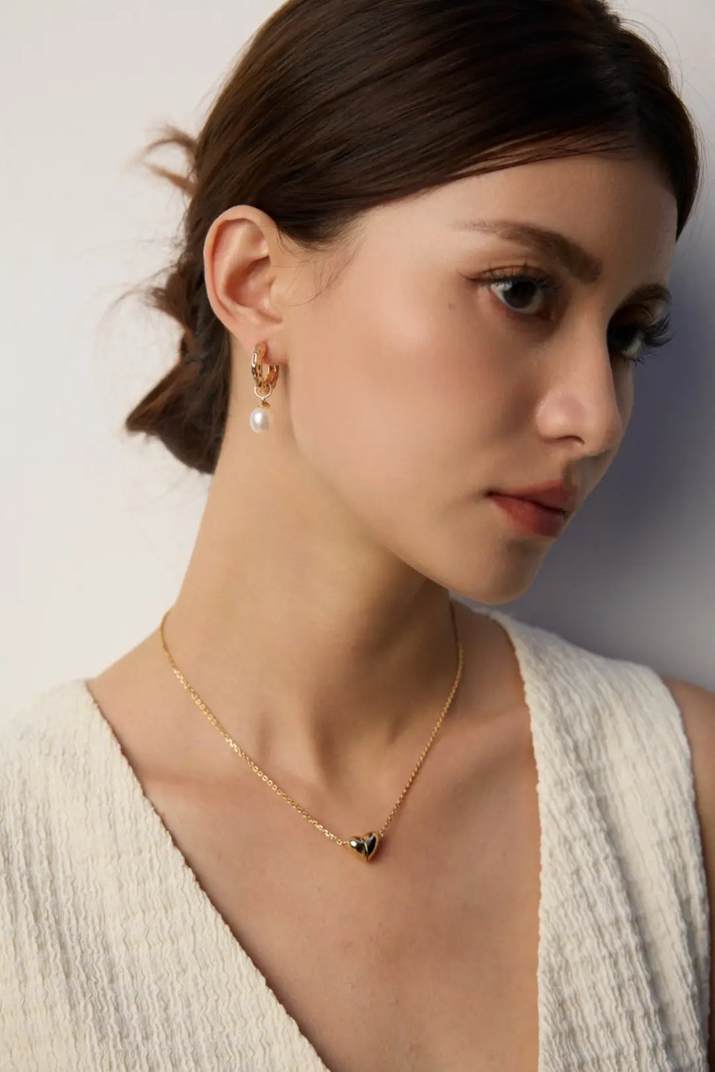 Woman wearing a gold necklace and earrings against a neutral background