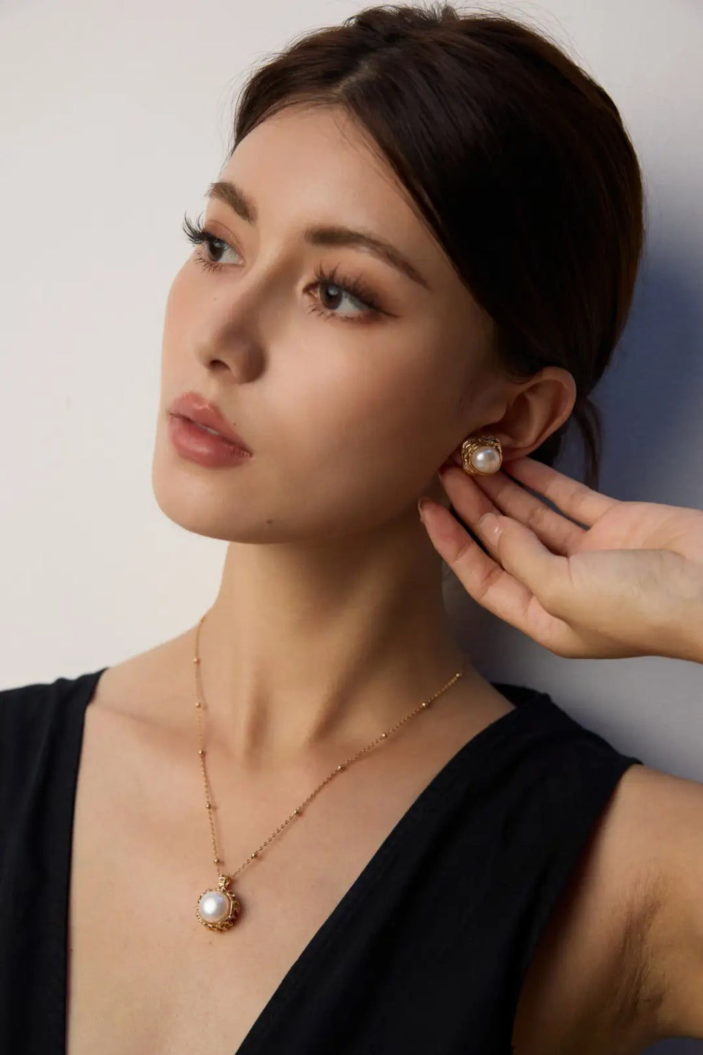 Woman wearing a pearl earring and necklace against a plain background