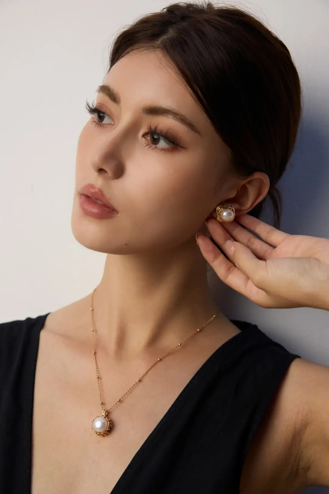 Woman wearing a pearl earring and necklace against a plain background