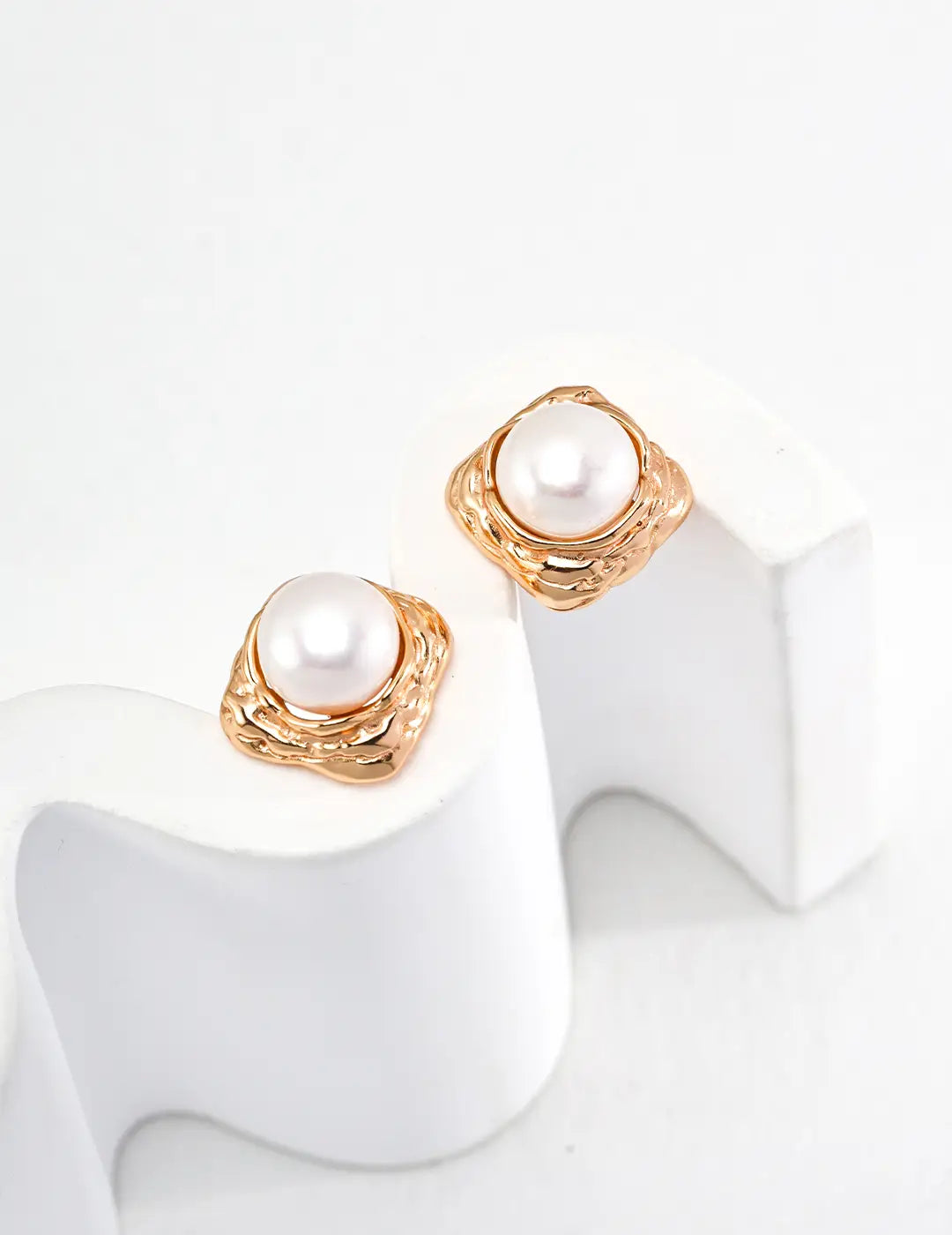 Pair of pearl earrings with gold accents on a white stand.