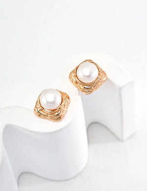 Pair of pearl earrings with gold accents on a white stand.