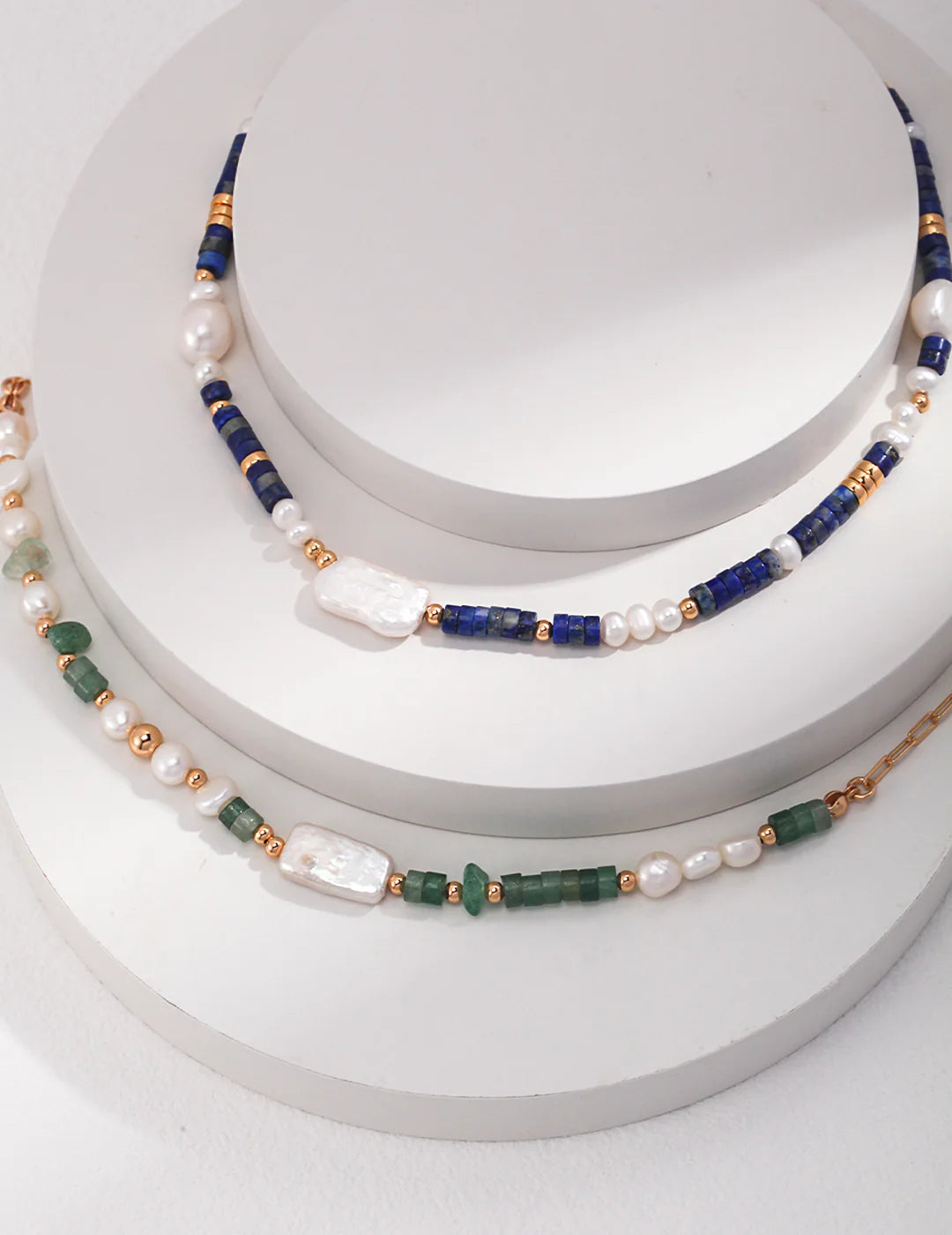 Two Navy Blue Lapis Lazuli and Baroque Pearl chokers on white stand.