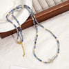 Camile Turquoise Lapis Lazuli Pendant Necklace with blue beads and gold accents, elegantly displayed on a white fabric next to a wooden box.