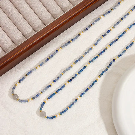 Two Camile Turquoise Lapis Lazuli Pendant Necklaces laid out in parallel on a soft white fabric, showcasing the vibrant blue beads and gold accents