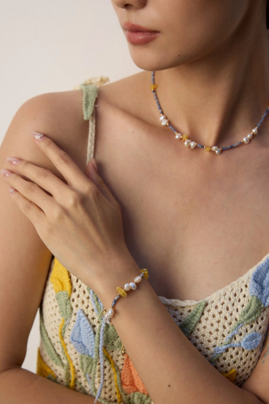 Close-up of woman’s hand wearing Celeste Harmony Bracelet with pearls and blue stones in soft light.