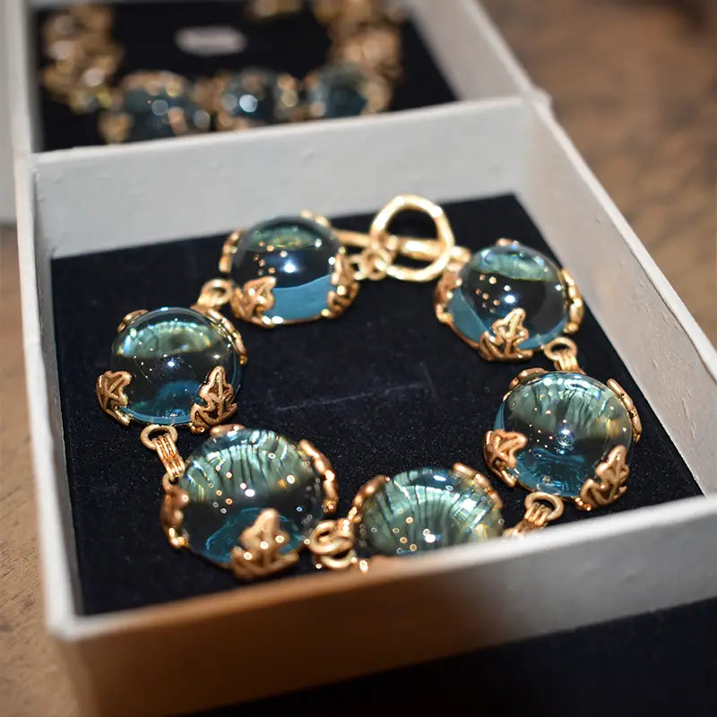 Close-up of the Patchouli Bristol Blue Glass Bracelet, showcasing round blue glass stones set in intricate gold leaf frames. The bracelet rests in a black velvet box, highlighting its vintage-inspired design and luxurious craftsmanship.