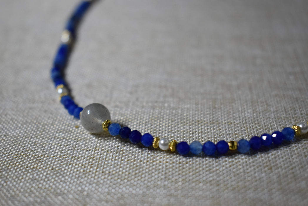 Detailed view of the Camile Turquoise Lapis Lazuli Pendant Necklace, showcasing the lapis lazuli beads and a round stone centerpiece on a neutral fabric background.