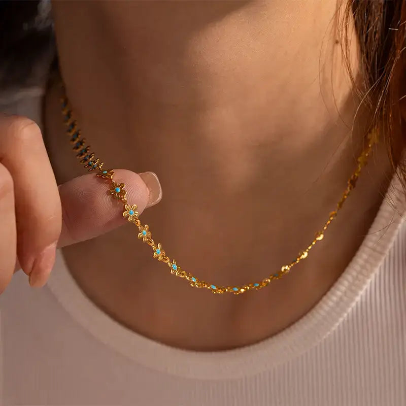Model wearing the Anais & Aimee Dainty Blue Flower Chain Necklace, featuring an intricate gold chain adorned with delicate blue flower accents. Perfect for adding a touch of elegance and femininity to any outfit.