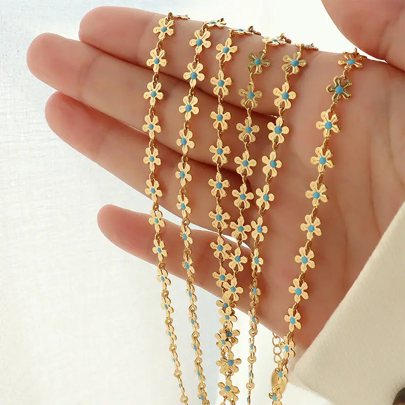 Hand holding the Anais & Aimee Dainty Blue Flower Chain Necklace, featuring an intricate gold chain adorned with delicate blue flower accents. Perfect for adding a touch of elegance and femininity to any outfit.