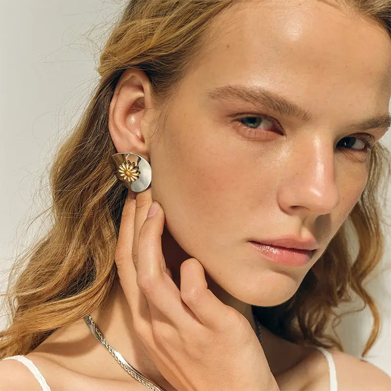 A woman wearing sterling silver daisy-shaped stud earrings with a sunbeam design on her ear.
