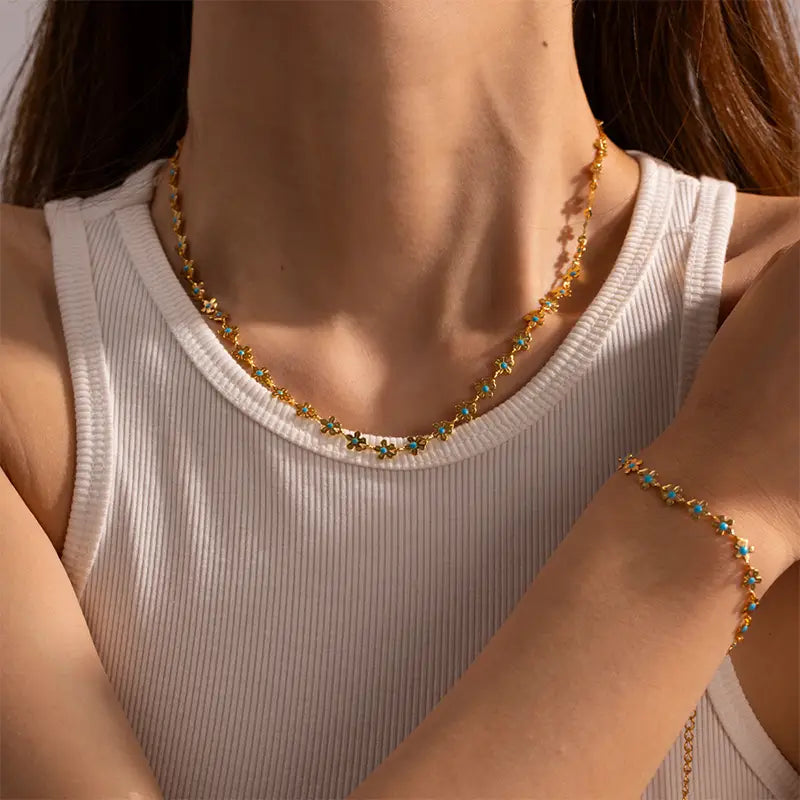 Model wearing the Anais & Aimee Dainty Blue Flower Chain Necklace and matching bracelet, featuring an intricate gold chain adorned with delicate blue flower accents. Perfect for adding a touch of elegance and femininity to any outfit.