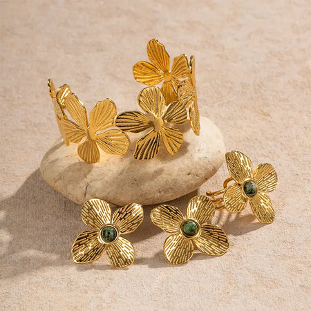 Anais & Aimee Dogwood Flower Collection featuring intricately designed gold-plated jewelry pieces, including a cuff bracelet and stud earrings adorned with genuine green gemstones. Perfect for adding a touch of natural elegance to any outfit.