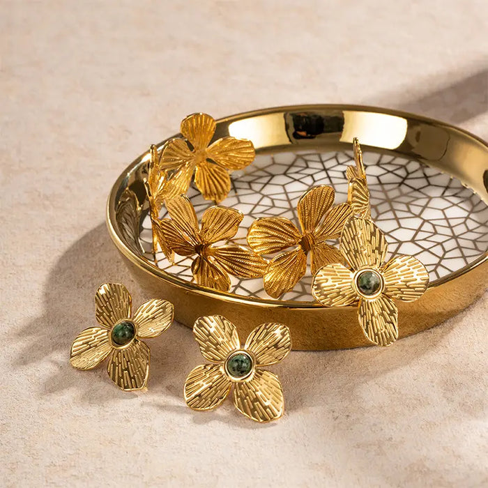Collection of Anais & Aimee Dogwood Flower Cuff Rings displayed in a golden dish, each featuring an 18K gold-plated base and a genuine green gemstone. The intricate petal designs symbolize rebirth and strength, offering elegant and timeless accessories.