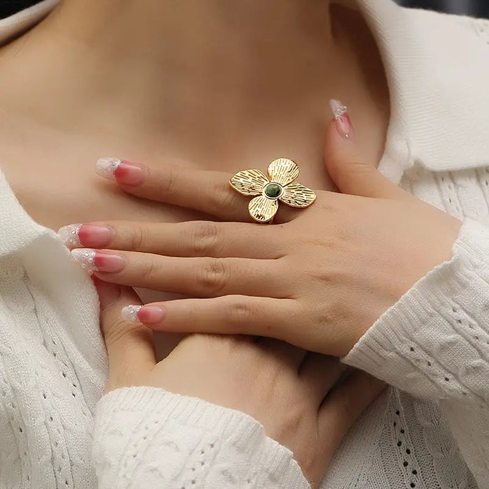 Woman wearing the Anais & Aimee Dogwood Flower Cuff Ring, featuring an 18K gold-plated base and a genuine green gemstone. The ring's intricate petal design symbolizes rebirth and strength, offering an elegant and timeless accessory for any outfit.