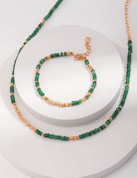 A close-up of the Emerald Green Necklace Choker with Gold Stones by Anaïs & Aimee, showcasing the vibrant green beads and shimmering gold accents on a delicate gold chain.