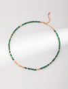 A full-length view of the Emerald Green Necklace Choker by Anaïs & Aimee, featuring an adjustable gold chain adorned with emerald green beads and gold stones.