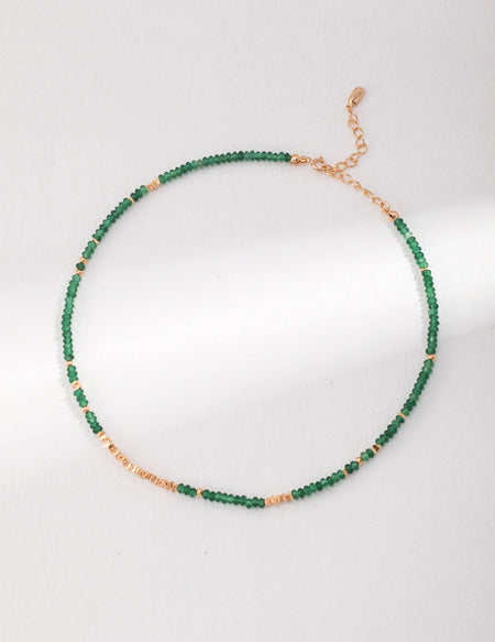 A full-length view of the Emerald Green Necklace Choker by Anaïs & Aimee, featuring an adjustable gold chain adorned with emerald green beads and gold stones.