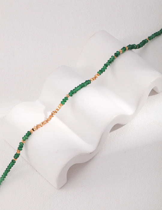 An elegant display of the Emerald Green Necklace Choker with Gold Stones by Anaïs & Aimee, artfully styled on a white curved stand to emphasize its intricate design.