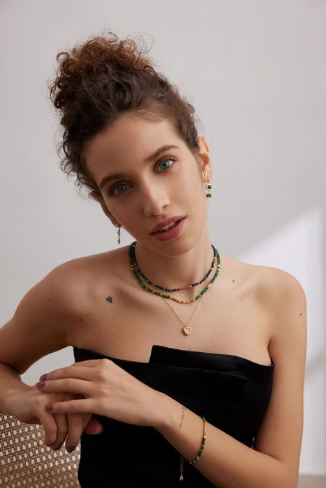 Model wearing the Emerald Green Necklace Choker with Gold Stones by Anaïs & Aimee, layered with other gold jewelry pieces, styled to highlight its timeless elegance.