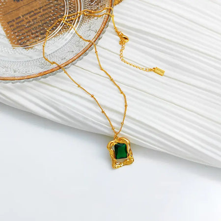 Elegant Evergreen Emerald Stud Necklace displayed on a textured surface, featuring a striking green crystal pendant encased in a polished gold-tone setting with an adjustable chain, perfect for adding a touch of sophistication and luxury to any ensemble.