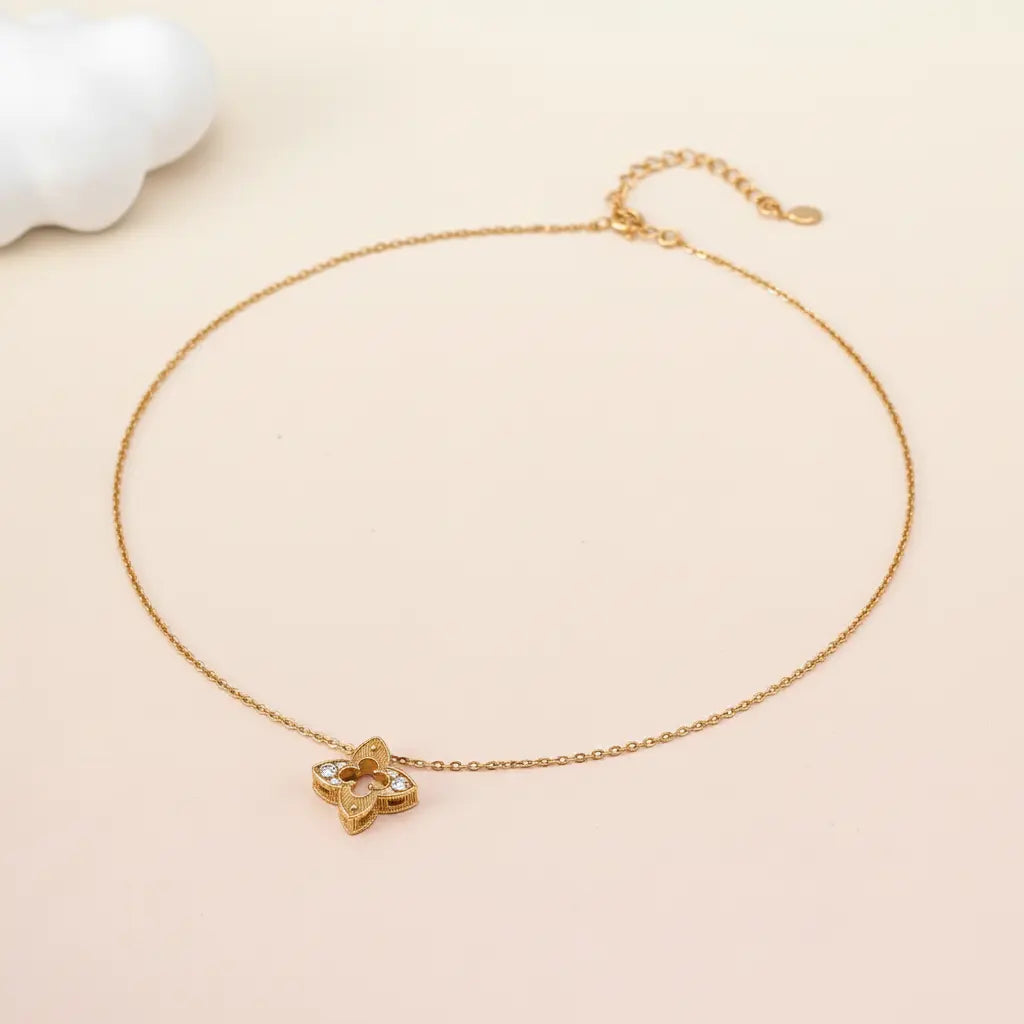 Gold necklace with a clover-shaped pendant on a beige background