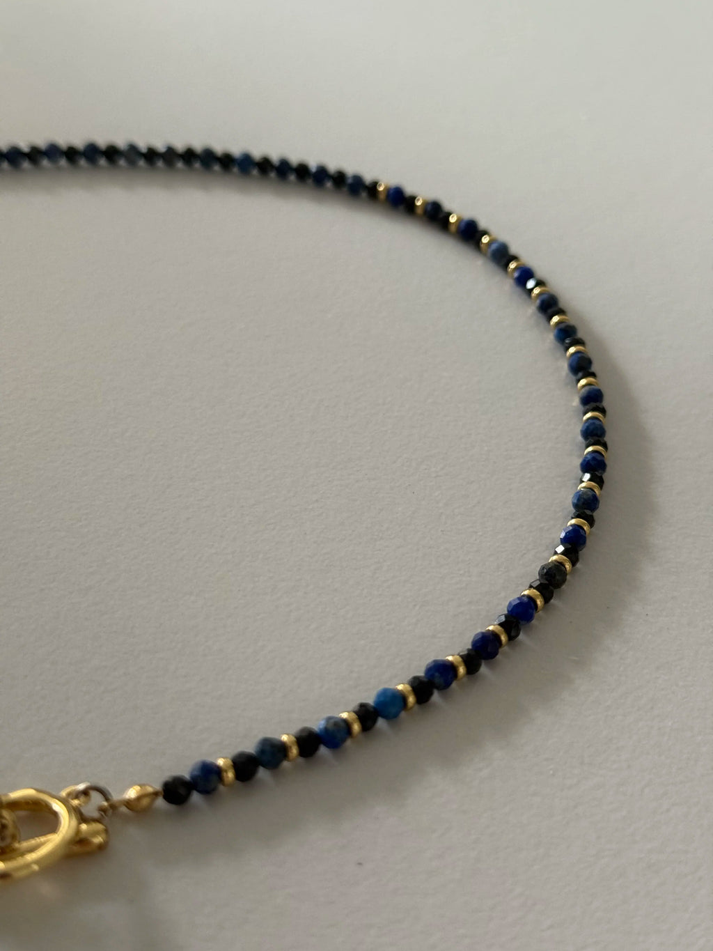 Detailed view of lapis lazuli and black spinel gemstone beads with faceted cuts and gold accents, highlighting the texture and contrast of the necklace.