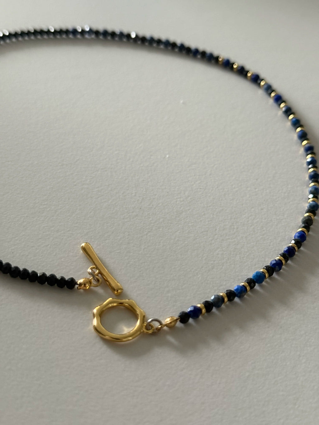Front view of the necklace’s toggle clasp in gold-tone, styled flat to show the beading pattern and construction.