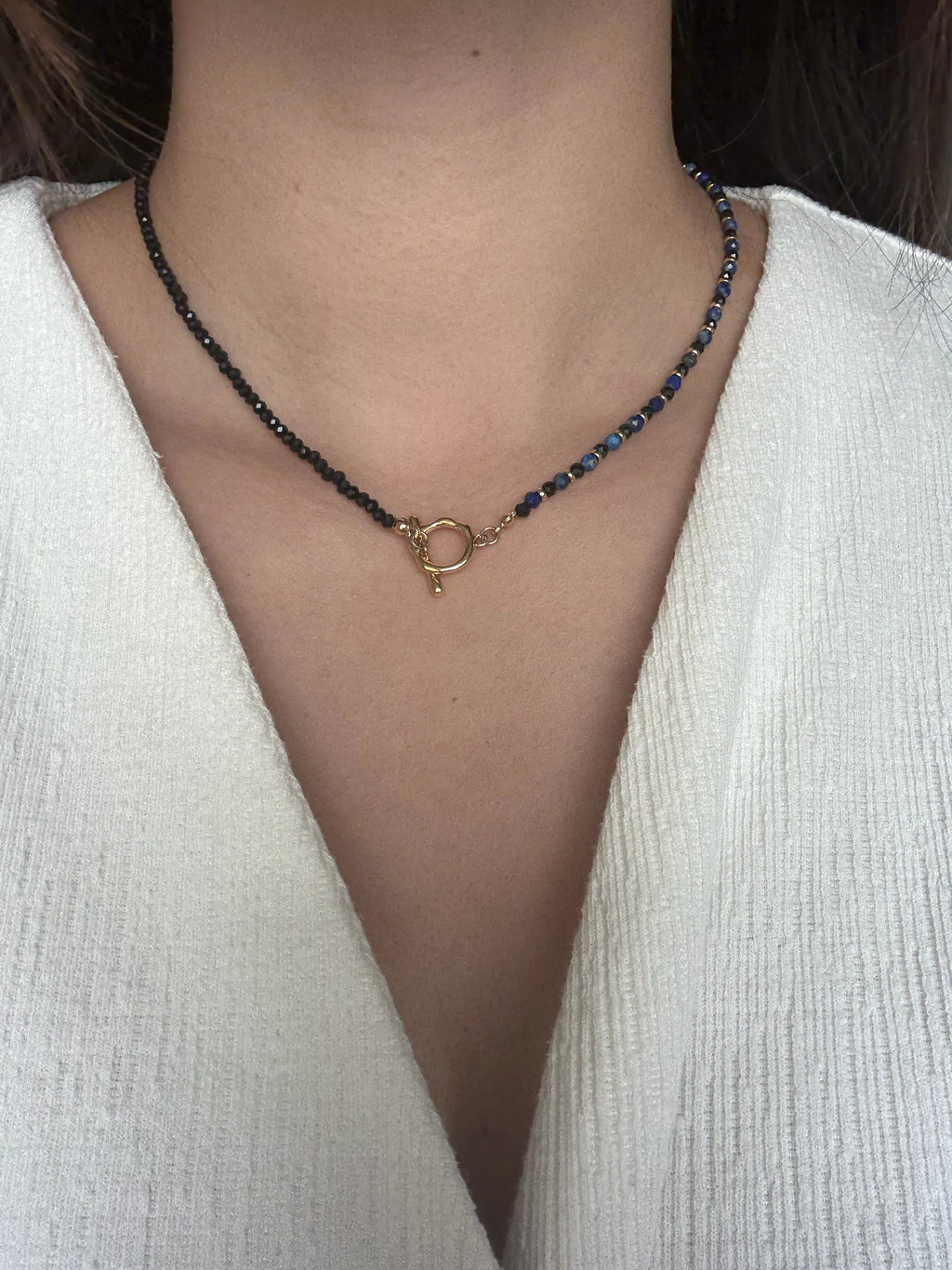 Angle shot of the full necklace laid flat, showing the symmetry and alternating gemstone colours with polished gold clasp details.

