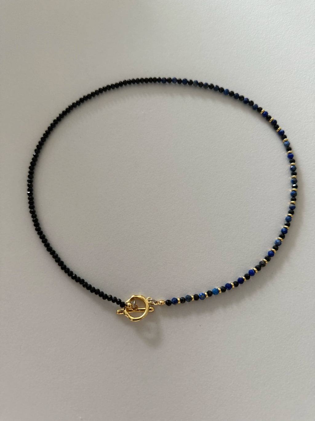 Close-up of the full Gempires Necklace featuring alternating 4mm lapis lazuli and black spinel beads with gold-tone spacers on a light backdrop.