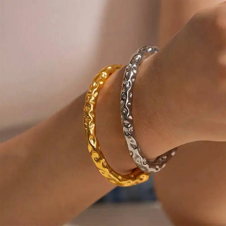 Hammer Gold Bracelet and a matching silver bracelet, each featuring a unique hammered texture with raised, organic patterns, worn on a wrist. These high trending accessories are perfect for making bold and sophisticated fashion statements, adding a touch of elegance to any ensemble.