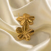 Pair of gold hibiscus flower earrings with detailed petals, displayed on a soft, ivory-colored fabric, showcasing their elegant and polished design.