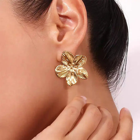Close-up of a model wearing a gold hibiscus flower earring with detailed petals, showcasing its elegant and polished design.