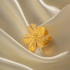 Gold ring featuring a detailed hibiscus flower design with polished petals, displayed on a soft, champagne-colored fabric, showcasing its side profile